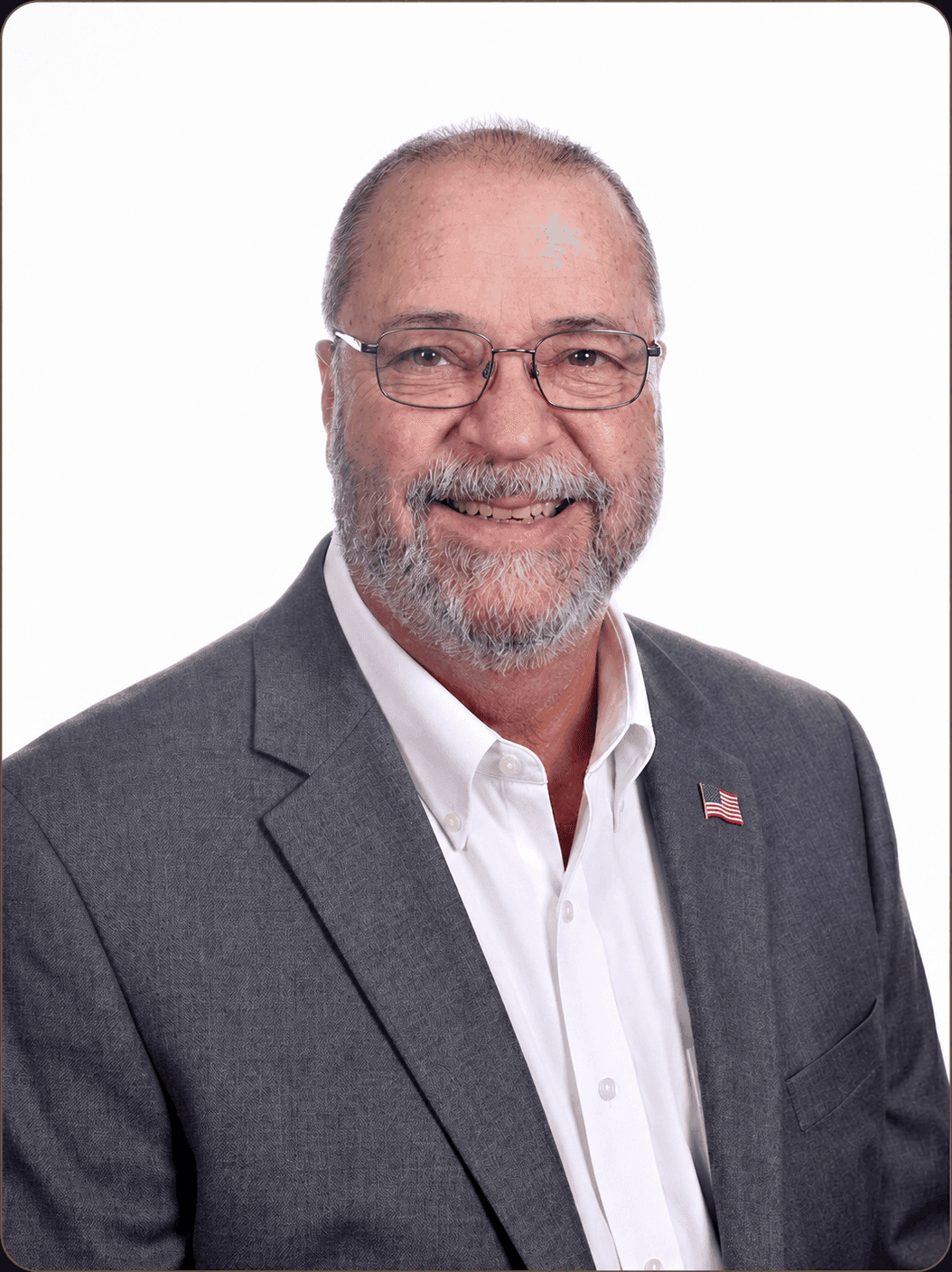 Steven Goddu, owner and production manager of Goddu Imprint, smiling in a gray suit jacket over an open-collar white shirt with an American flag lapel pin.